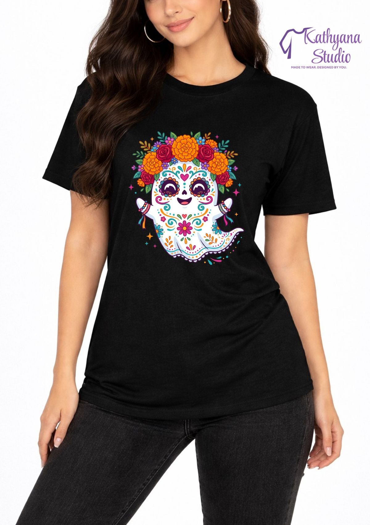 A woman wearing a black short-sleeve t-shirt with a colorful sugar skull ghost graphic on the front, paired with black jeans. The 'Kathyana Studio' brand logo is visible in the top right corner.
