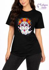 A woman wearing a black short-sleeve t-shirt with a colorful sugar skull ghost graphic on the front, paired with black jeans. The 'Kathyana Studio' brand logo is visible in the top right corner.